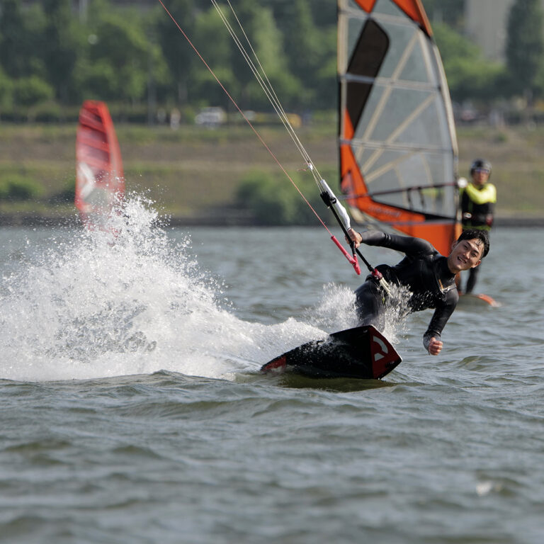 Kitesurfer flying over the flat Han river water in the centre of Seoul. Smiling man doing toe side riding while kitesurfing, kiteboarding in Seoul South Korea
