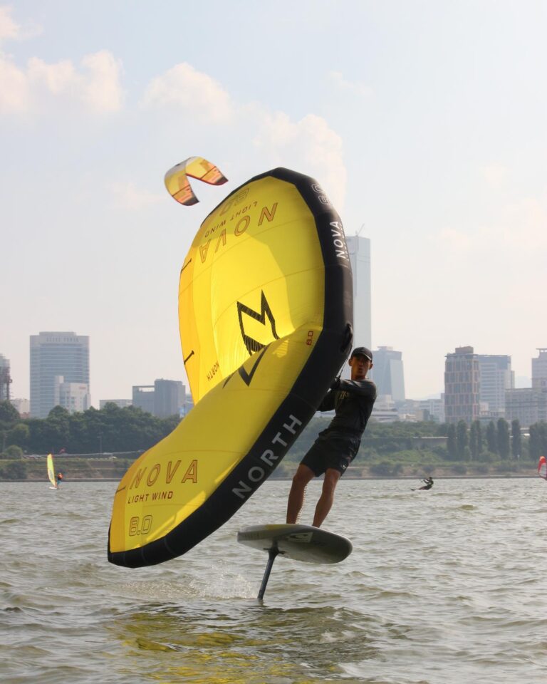 wing foiler practicing wing foiling on the Han river in the middle of Seoul, South Korea. Enjoying water sport in South Korea, On the flat waters of the Hangang. Riding his foil board with the scenic view of Korean skyscrapers on the background. This makes a perfect and active activity in Seoul.
