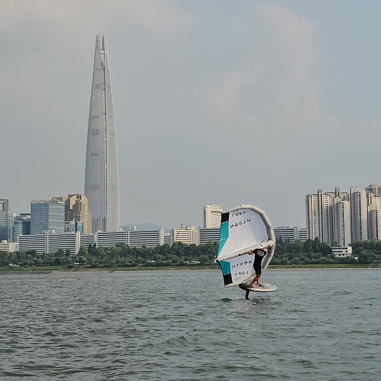 wing foiler in hangang with the Lotte tower in the background. Enjoying watersports in Seoul with their rental wing foil gear from North. Getting wing foil lessons in Seoul South Korea