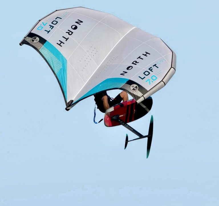 Wing Foiler flying in the air in front of our Vietnam Kite shop in Phan Rang. Vietnam winter camp. Wing foil Jeju island South Korea. Wing foil instructor flying with new gear above the water with the blue sunny sky as a background.