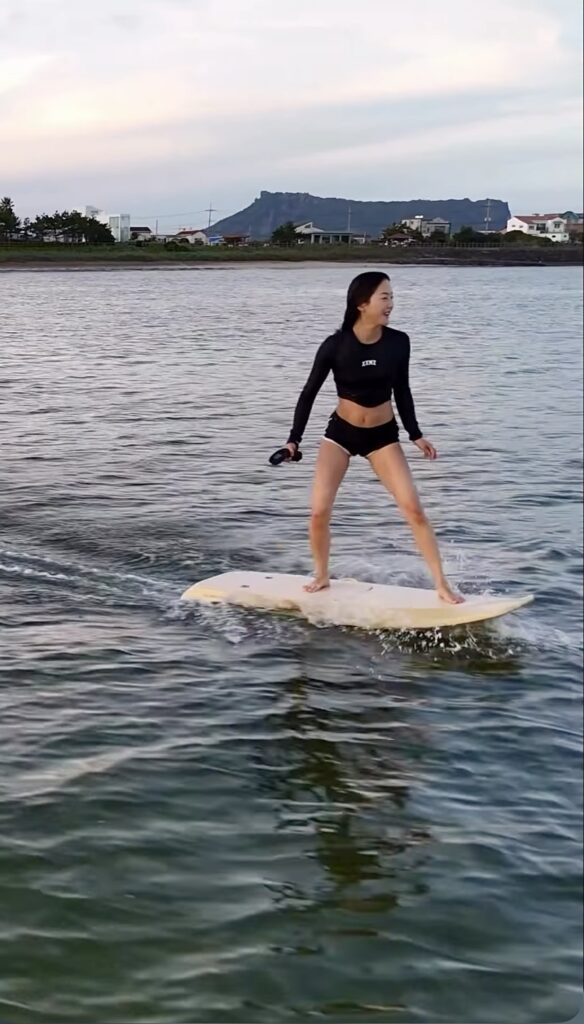 woman eFoiling on Jeju island with sunrisepeak in the background. Enjoying watersports in Jeju island South Korea. Riding a Pulseer E-Foil in South Korea